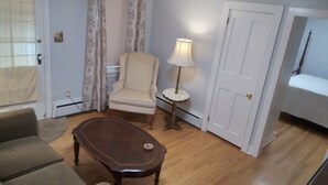 A room with a wooden floor, a beige armchair, a dark wooden coffee table, a small round table with a lamp, and a bed with a patterned bedspread. - Apartment for the traveling professional (Bristol)