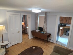 A room with a wooden floor, a table with a lamp, a chair, and a small table with books. There is a door leading to another room. - Apartment for the traveling professional (Bristol)