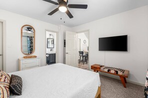 A bedroom with a bed, a dresser, a mirror, a ceiling fan, and a TV on the wall. - Castaway Beach Bungalow Pets Welcome (Surfside Beach)