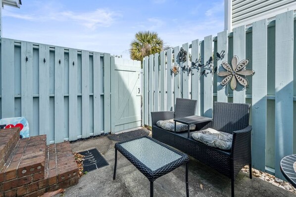 Eine Terrasse mit einer Rattan-Couch, einem kleinen Tisch und einer Wanddekoration mit einem Schmetterling.