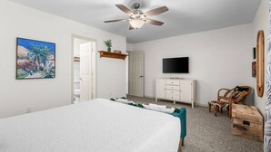 Ein Schlafzimmer mit Bett, Fernseher, Deckenventilator und einer Tür zu einem anderen Raum.
