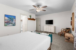 Ein Schlafzimmer mit Bett, Fernseher, Deckenventilator und einer Tür zu einem anderen Raum.