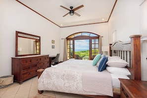 A bedroom with a large bed, a dresser, a mirror, and a view of the outdoors.