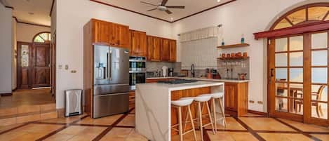 A spacious kitchen with a central island, wooden cabinets, stainless steel appliances, and a large window.