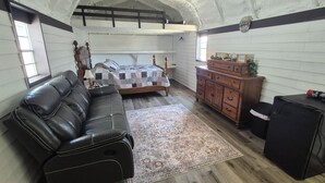 Een kamer met een bed, een houten dressoir, een zwarte leren bank en een klein zwart kastje.