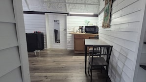Een smalle gang met een houten vloer die uitkomt in een keuken met een houten tafel en stoelen.