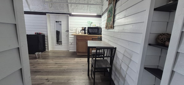 A narrow hallway with a wooden floor leading to a kitchen area with a wooden table and chairs.