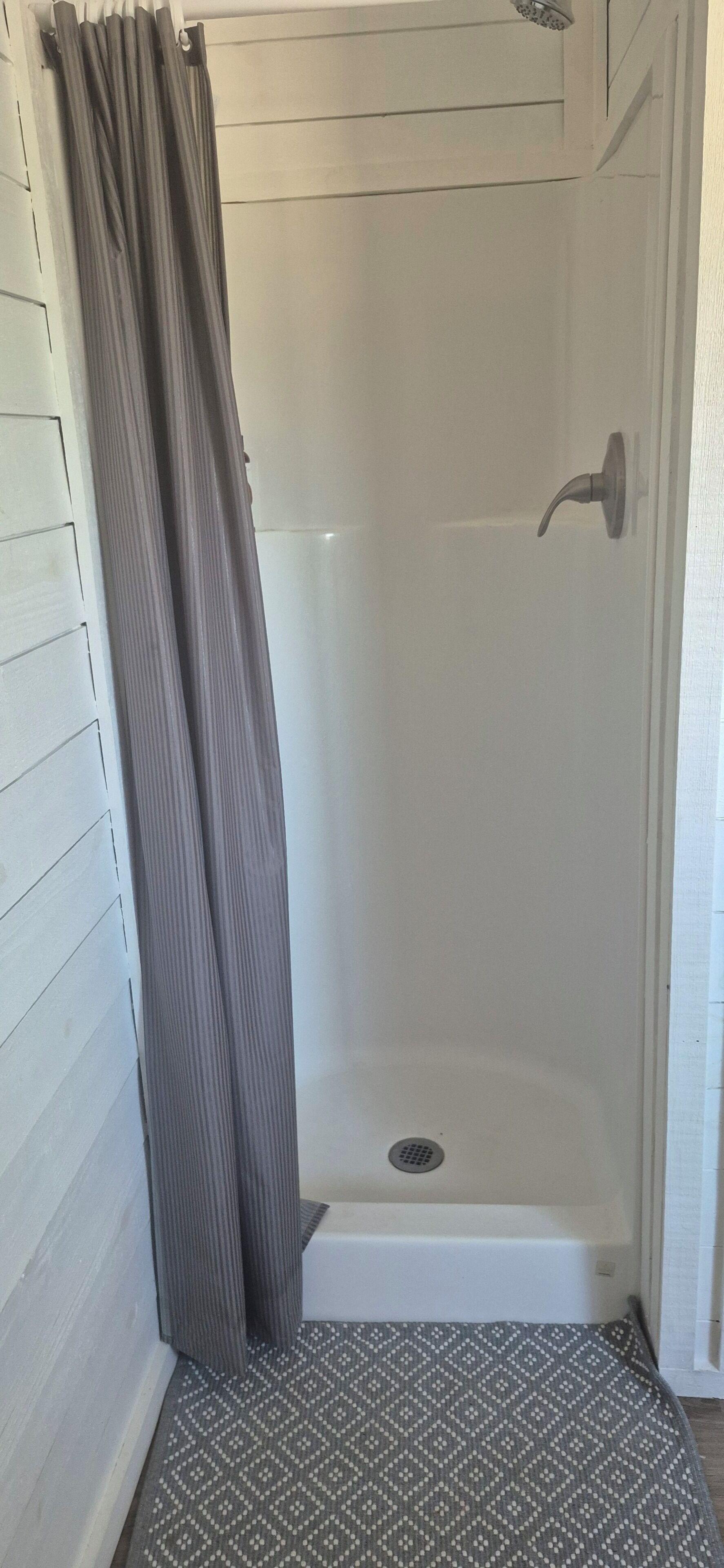 A shower area with a shower curtain, a showerhead, and a drain.