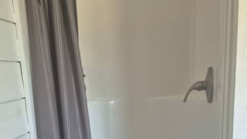 A shower area with a shower curtain, a showerhead, and a drain.