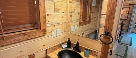 A wooden cabin-style bathroom with a wooden sink, a mirror, and a towel rack.