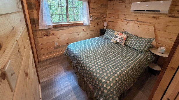 Ein Schlafzimmer einer Holzhütte mit einem Bett, einem Fenster und einer Klimaanlage.