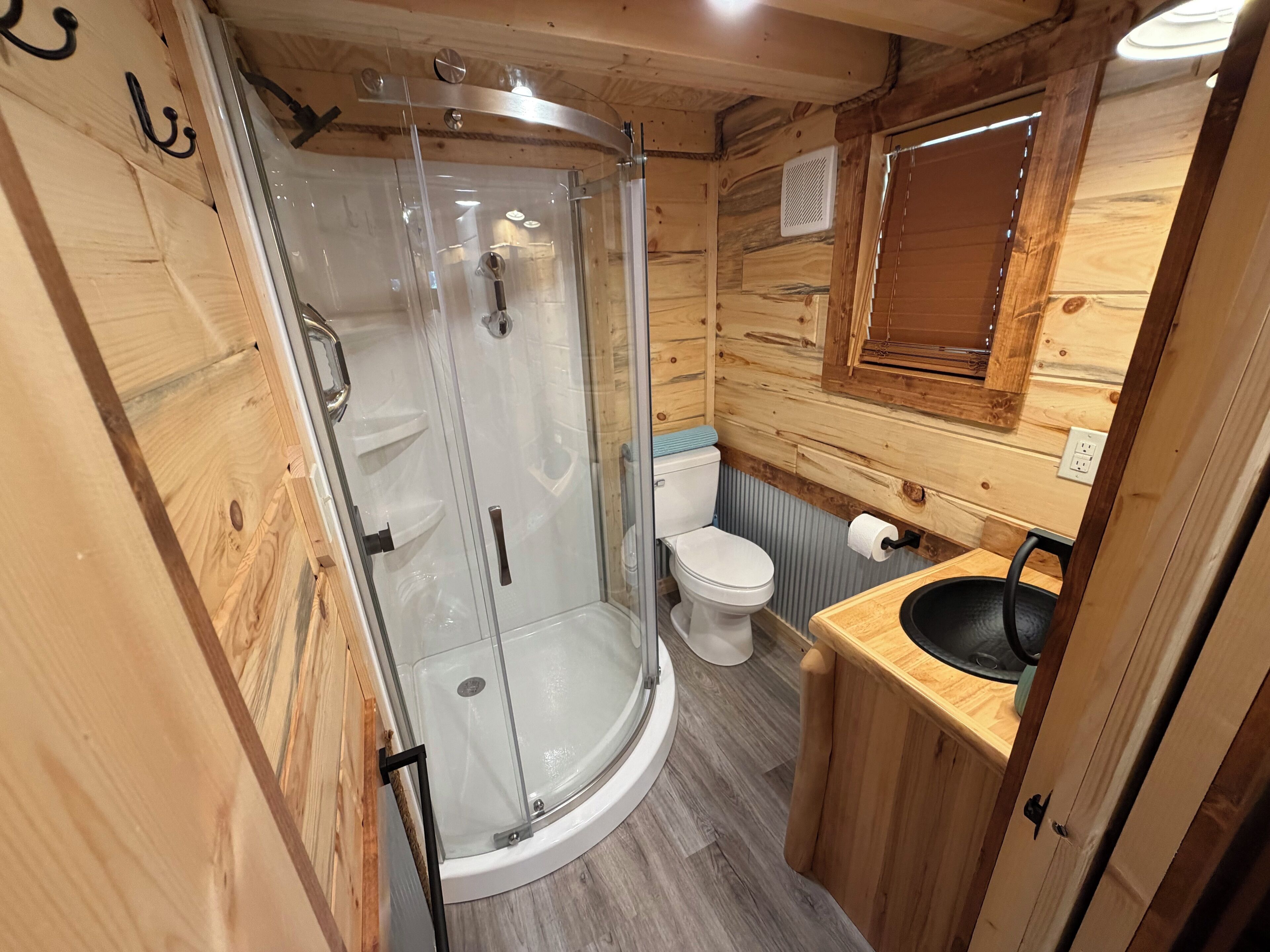 A wooden interior with a glass-enclosed shower, a white toilet, and a wooden sink.