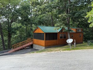 A wooden cabin with a green roof, a wooden deck, and a small staircase leading to a porch.
