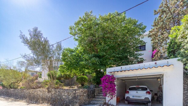 Un edificio blanco con un garaje, un muro de piedra y un árbol de follaje verde.