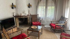 Una sala de estar con chimenea, televisor y dos sillones de mimbre con cojines rojos.