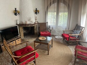 Ein Wohnzimmer mit Kamin, Fernseher und zwei Korbstühlen mit roten Kissen.