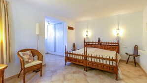 Un dormitorio con una cama doble de madera, una silla de mimbre, una lámpara de pie y vistas al exterior.
