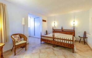 Ein Schlafzimmer mit einem Doppelbett aus Holz, einem Korbstuhl, einer Stehlampe und Blick ins Freie.