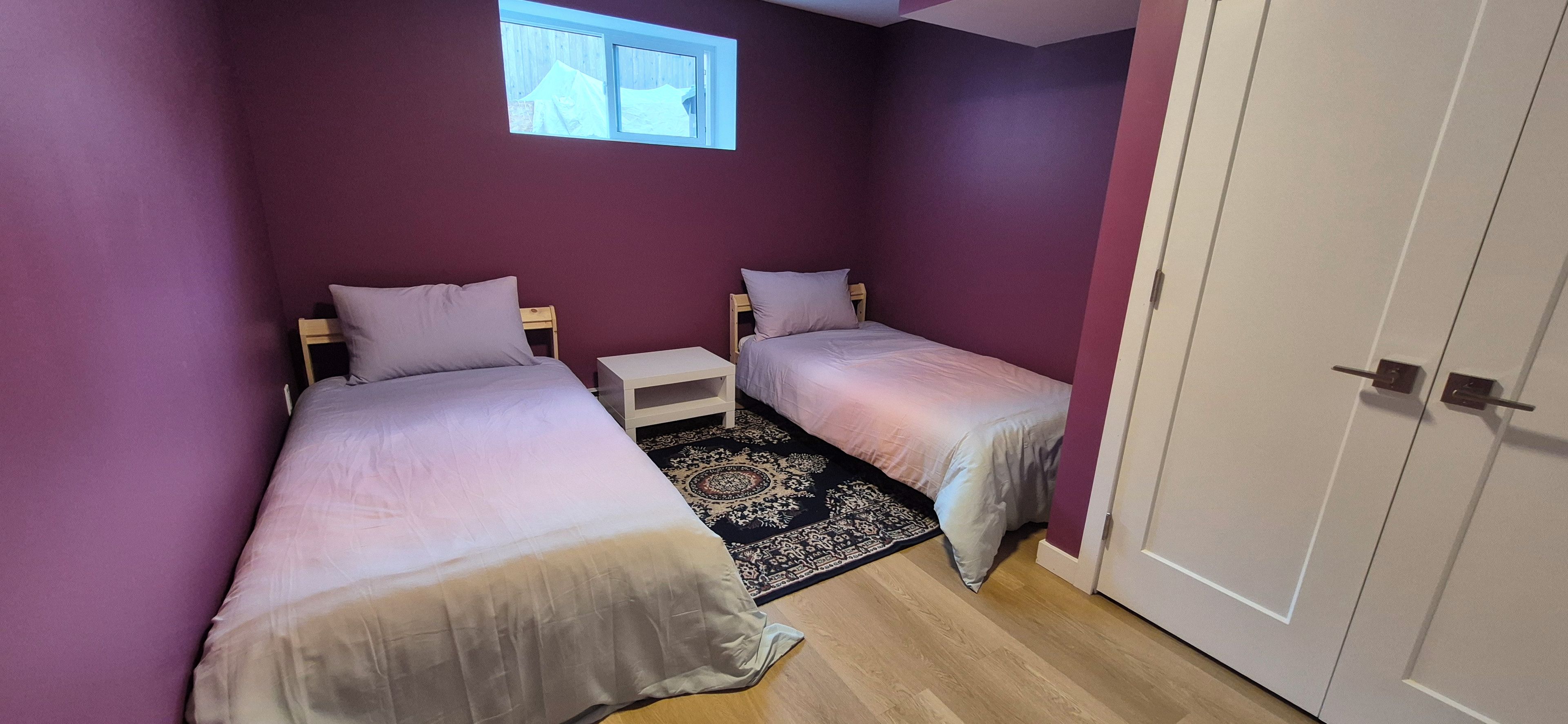 A bedroom with two beds, a small bedside table, a rug, and a window.