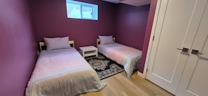A bedroom with two beds, a small bedside table, a rug, and a window.