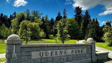 A stone wall with 'QUEEN'S PARK' engraved, surrounded by greenery and trees.