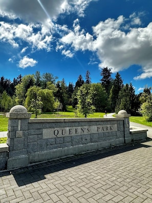 A stone wall with 'QUEEN'S PARK' engraved, surrounded by greenery and trees.