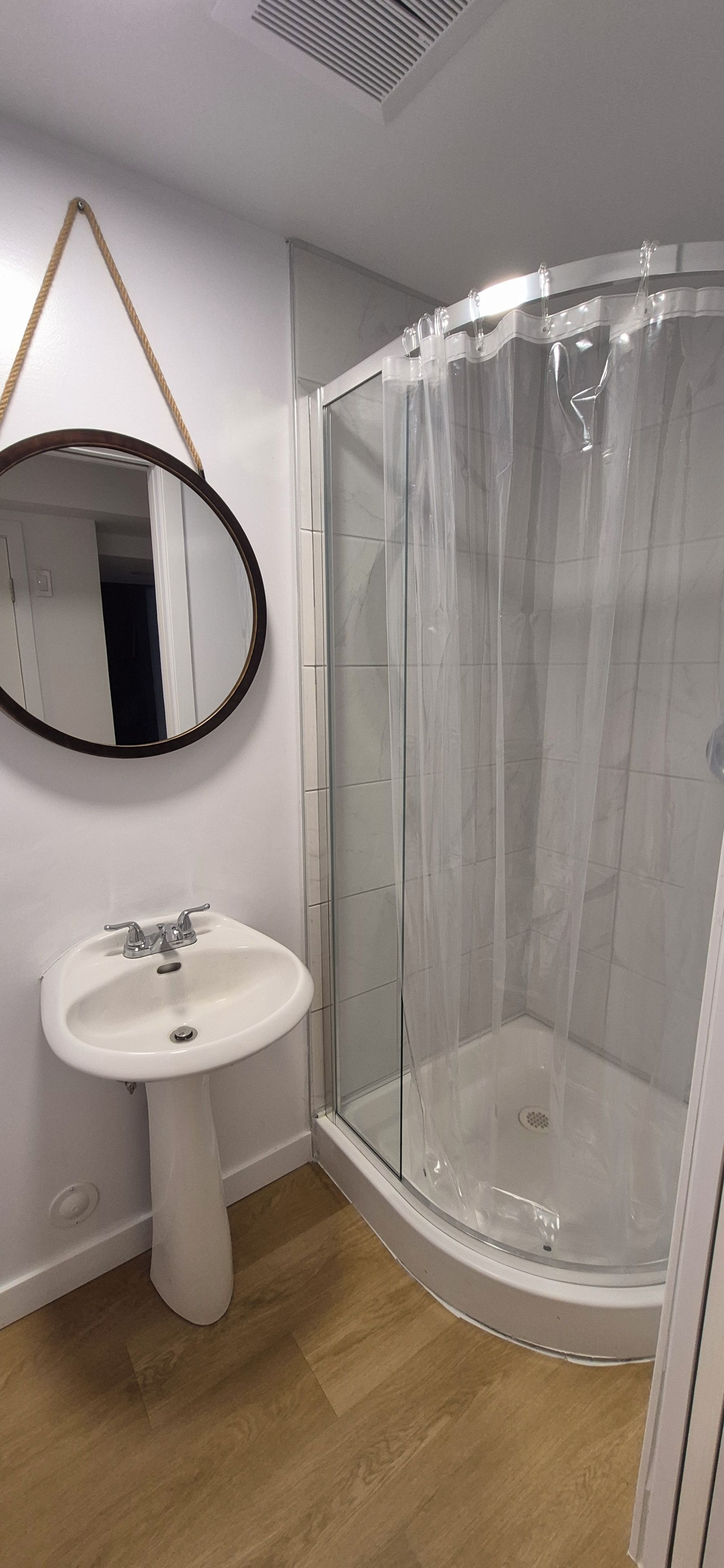 A bathroom with a white pedestal sink, a glass shower enclosure, and a mirror with a rope handle.