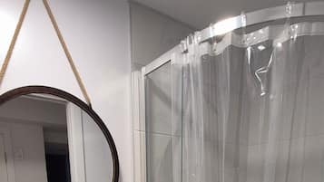 A bathroom with a white pedestal sink, a glass shower enclosure, and a mirror with a rope handle.