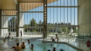 An indoor swimming pool with clear glass walls, a tiled floor, and a view of trees outside.
