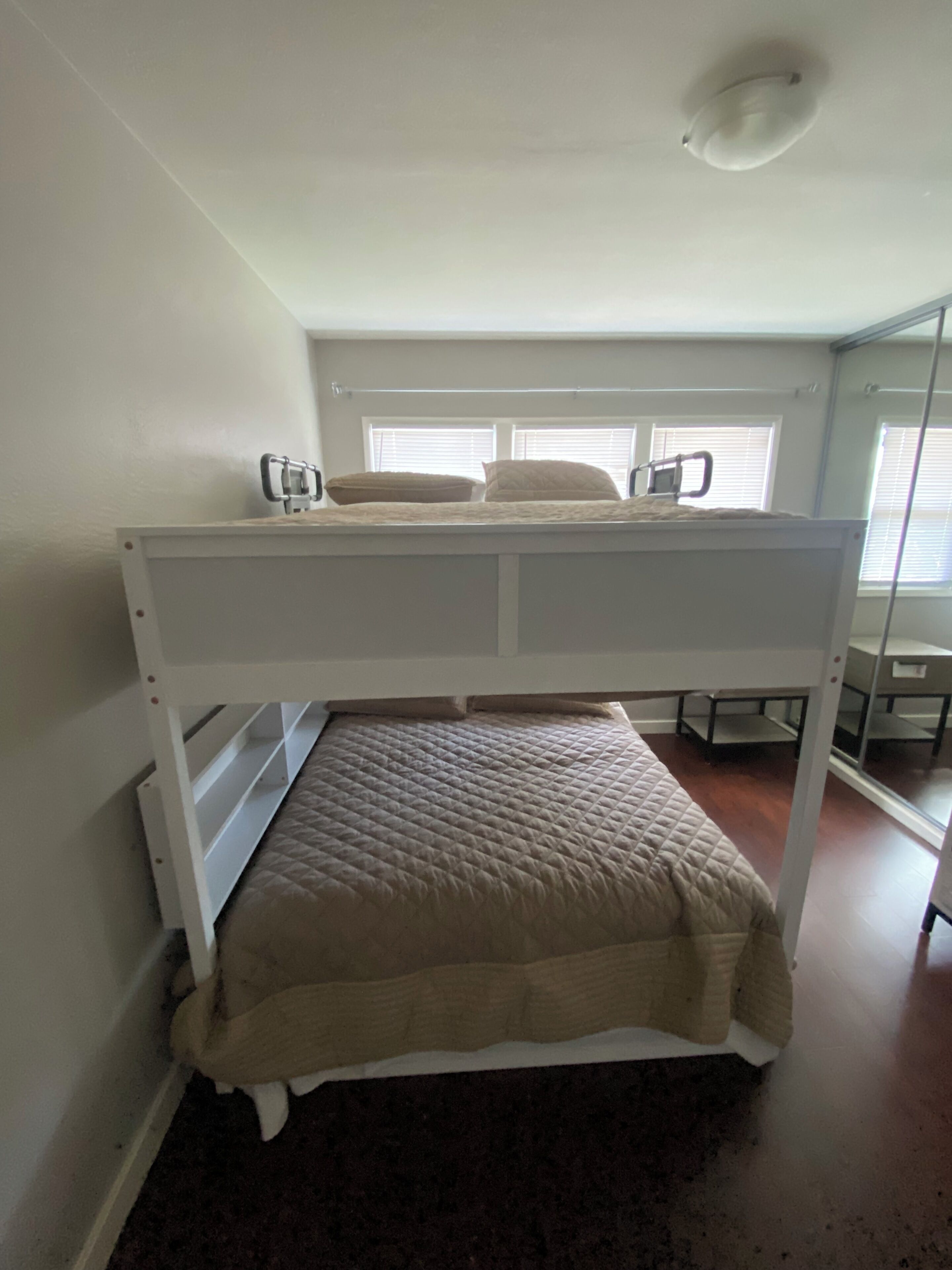 Una cama litera con colchón y almohadas, una ventana con persianas y una lámpara en el techo.