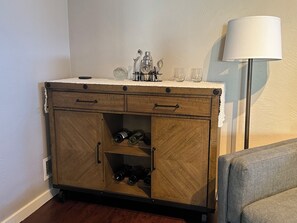 Eine Holzkommode mit zwei Schubladen, einem Weinkühler, einer Lampe und einem Stuhl.