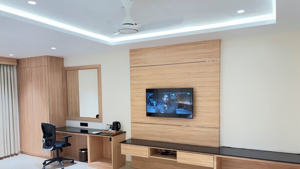 Habitación de hotel moderna con un televisor de pantalla plana grande montado en una pared de madera, un escritorio con una silla y un ventilador de techo.