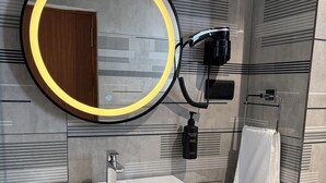 Un baño moderno con un lavamanos blanco, un espejo redondo con marco amarillo y un perchero para toallas.
