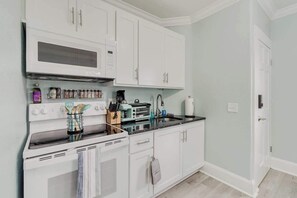 A kitchen with white cabinets, a microwave, a stove, and various kitchen utensils. - Quiet Palm Loft Near Lake w/ BBQ & Patio (Lakeland)