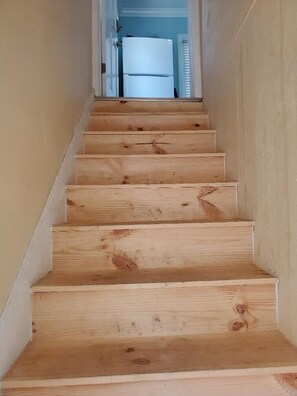 Eine Holztreppe führt zu einem Raum mit einer weißen Tür und einem Fenster mit Jalousien.