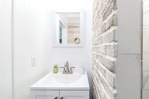 A bathroom with a white sink, a mirror, and a brick wall. - Quiet Palm Loft Near Lake w/ BBQ & Patio (Lakeland)