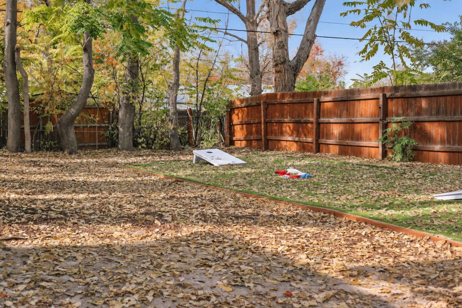 Une cour arrière avec une clôture en bois, un sol recouvert de feuilles et un objet blanc sur l’herbe.