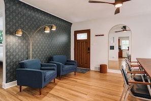 A living room with a dark patterned wallpaper, two blue armchairs, a wooden dining table with chairs, and a ceiling fan. - 2bd 1 Bth Apt. (Denver)