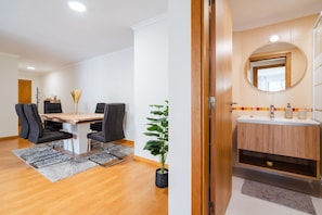 Ein modernes Hotelzimmer mit einem Holztisch, schwarzen Stühlen, einem Topf mit Pflanze, einem Schminktisch aus Holz mit Spiegel und einem kleinen Fenster.