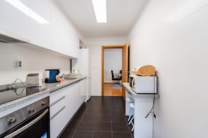 Een moderne keuken met witte kasten, een granieten aanrechtblad, een inbouwoven en een magnetron.