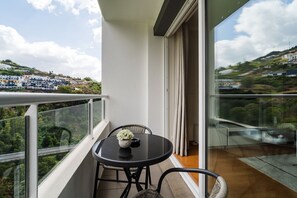 A balcony with a table and chairs, a potted plant, and a view of a hillside with buildings. - GuestReady - Family apartment with pool (Caniço)