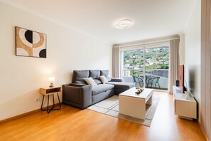 Een moderne woonkamer met een grijze bank, een klein wit bijzettafeltje en een televisie op een meubel.