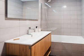 A modern bathroom with a white sink, wooden vanity, and a bathtub. - GuestReady - Family apartment with pool (Caniço)