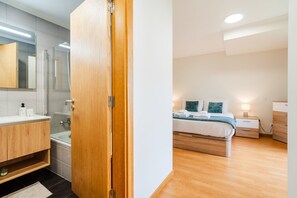 A modern bedroom with a wooden door, a bed with white bedding, a nightstand, and a bedside table. - GuestReady - Family apartment with pool (Caniço)