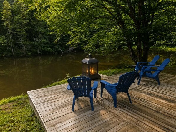 Una terraza de madera con una mesa, sillas, un farol y un lago.