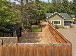Eine Holzterrasse mit einem eingezäunten Bereich, eine kleine Holzhütte und ein Haus mit grüner Dachbegrünung.