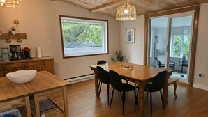 A dining area with a wooden table and chairs, a hanging light fixture, and a view through a large window. - A beautiful cabin with a private lake. (Saint-Cã´Me)