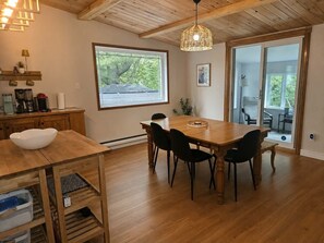 Ein Essbereich mit Holztisch und -stühlen, einer Hängelampe und Blick durch ein großes Fenster.