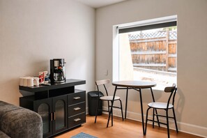 A compact living space with a kitchenette, a dining area with two chairs, a sofa, and a window with a view of a wooden fence. - 2Bd 1Bth Apt. | 100"TV | 3GB WIFI (Denver)
