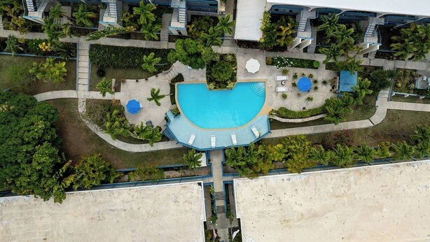 An aerial view of a hotel with a swimming pool, multiple balconies, and lush landscaping. - Caribbean Blue Hideaway | 1BR Condo w/ Ocean View (Christiansted)
